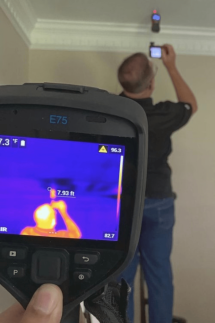 Man Standing on Ladder As Thermal Imaging Scanner Points to Ceiling